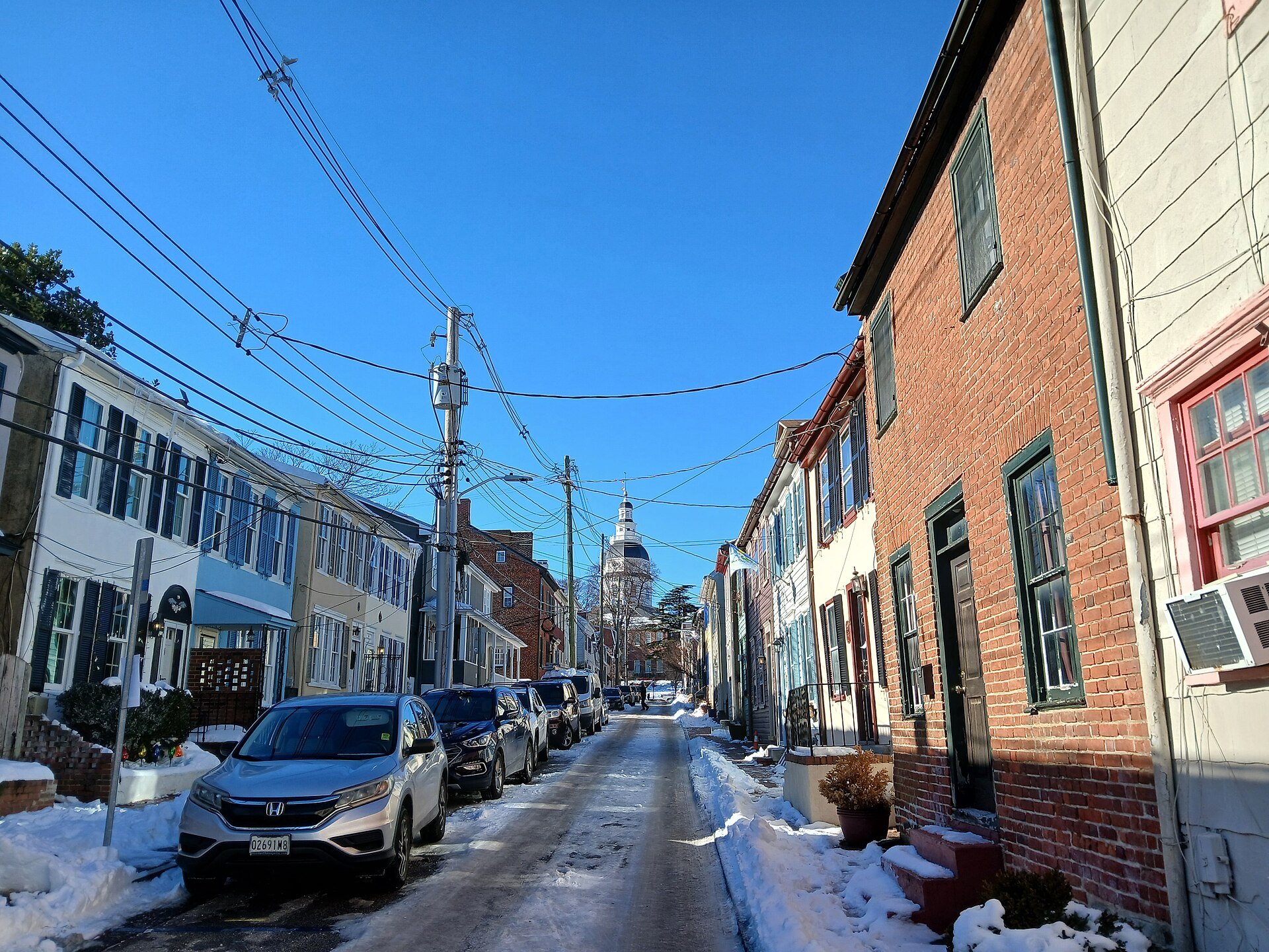 A snowy street of old houses in Annapolis, the State House dome at its end