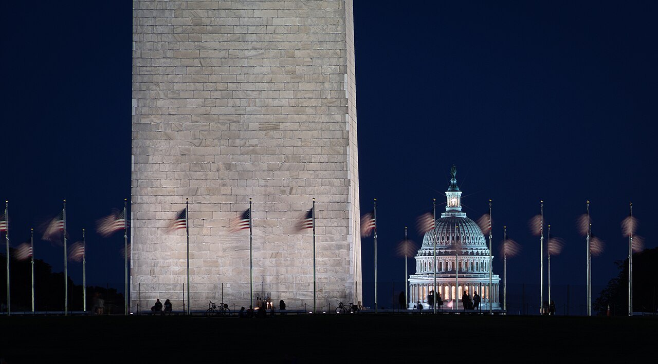 The Capitol dome, lit at night, beside the base of the Washington Monument