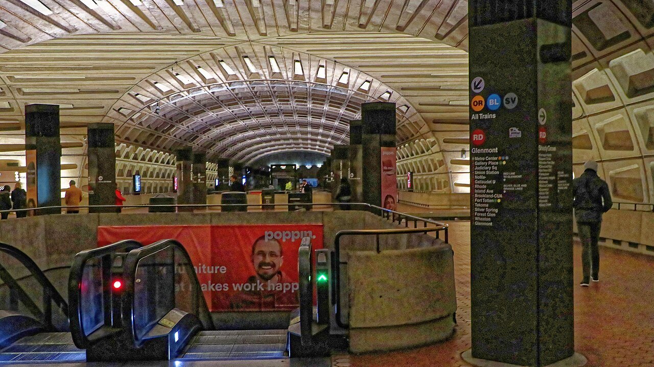 A Metro station mezzanine under the coffered concrete vault, escalators leading down