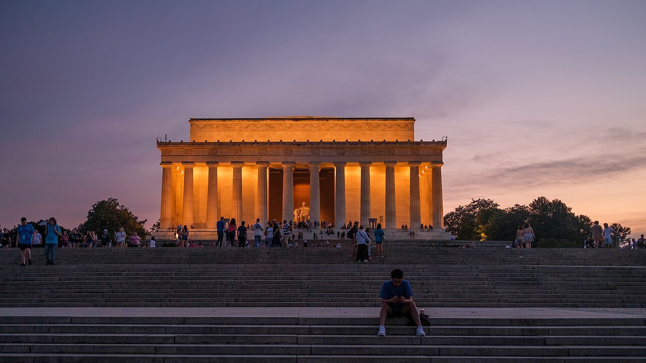 The Lincoln Memorial lit at dusk, a visitor sitting on the steps