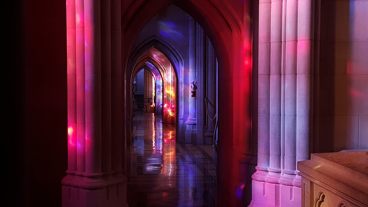 Stained glass casting red and blue light on the stone of the cathedral's nave